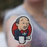 Hand holding a Jenkins sticker outdoors, blurred background for focus effect.